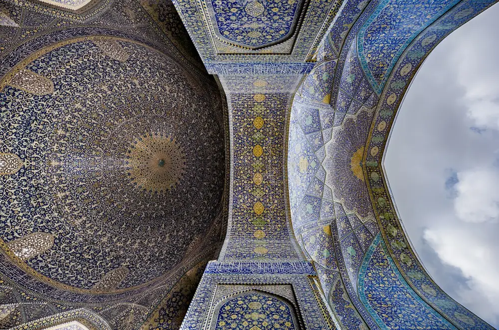 Looking straight up at the blue and gold tiled dome and arches of the Shah Mosque in Isfahan.